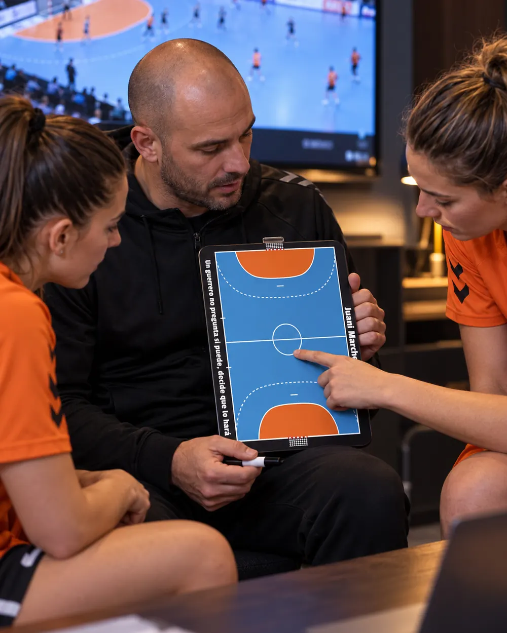 Een handbaltrainer neemt met zijn speelsters de tactiek door op het coachbord